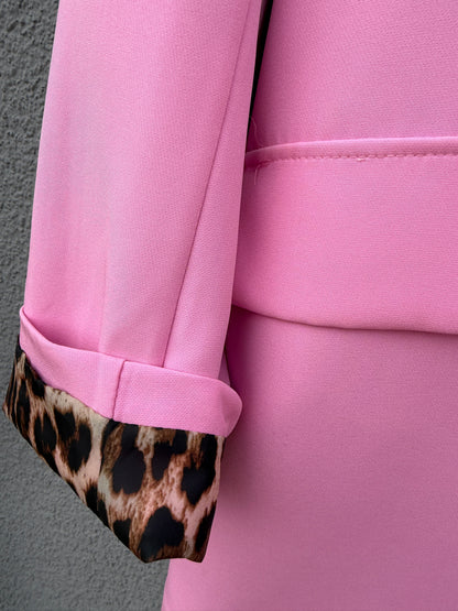 Eine Nahaufnahme des Feinraummode Eleganter Nice Fit Blazers in rosa mit Leopardenprint, mit hochgekrempeltem Ärmelbund, der das schicke Futter mit Leopardenprint vor einer strukturierten grauen Wand zeigt.