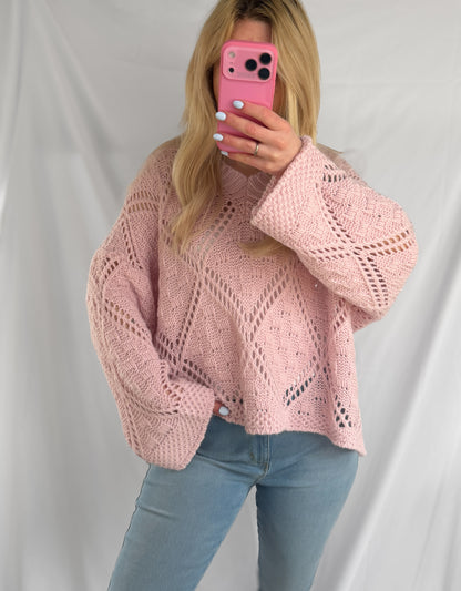 Eine Frau mit langen blonden Haaren trägt den Feinraummode Oversize Pullover Christina - einen rosa Damen Strickpullover im lässigen Oversize Look - und hellblaue Jeans und hält ein rosa Handy für ein Spiegel-Selfie vor einem weißen Hintergrund.