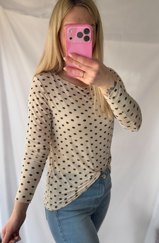 Eine Frau mit langen blonden Haaren macht ein Spiegel-Selfie in der Feinraummode Gepunktetes Cashmere Longsleeve - Polka Dots rosa & wollweiß, gepaart mit hellblauen Jeans. Ihr Gesicht ist teilweise hinter einem rosa Telefon verborgen.