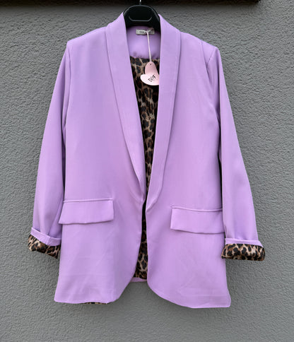 Der elegante Nice Fit Blazer in Flieder mit Leopardenprint von Feinraummode hängt an einem schwarzen Bügel vor grauer Wand, die Ärmel sind hochgekrempelt und am Kragen befindet sich ein herzförmiges Etikett.