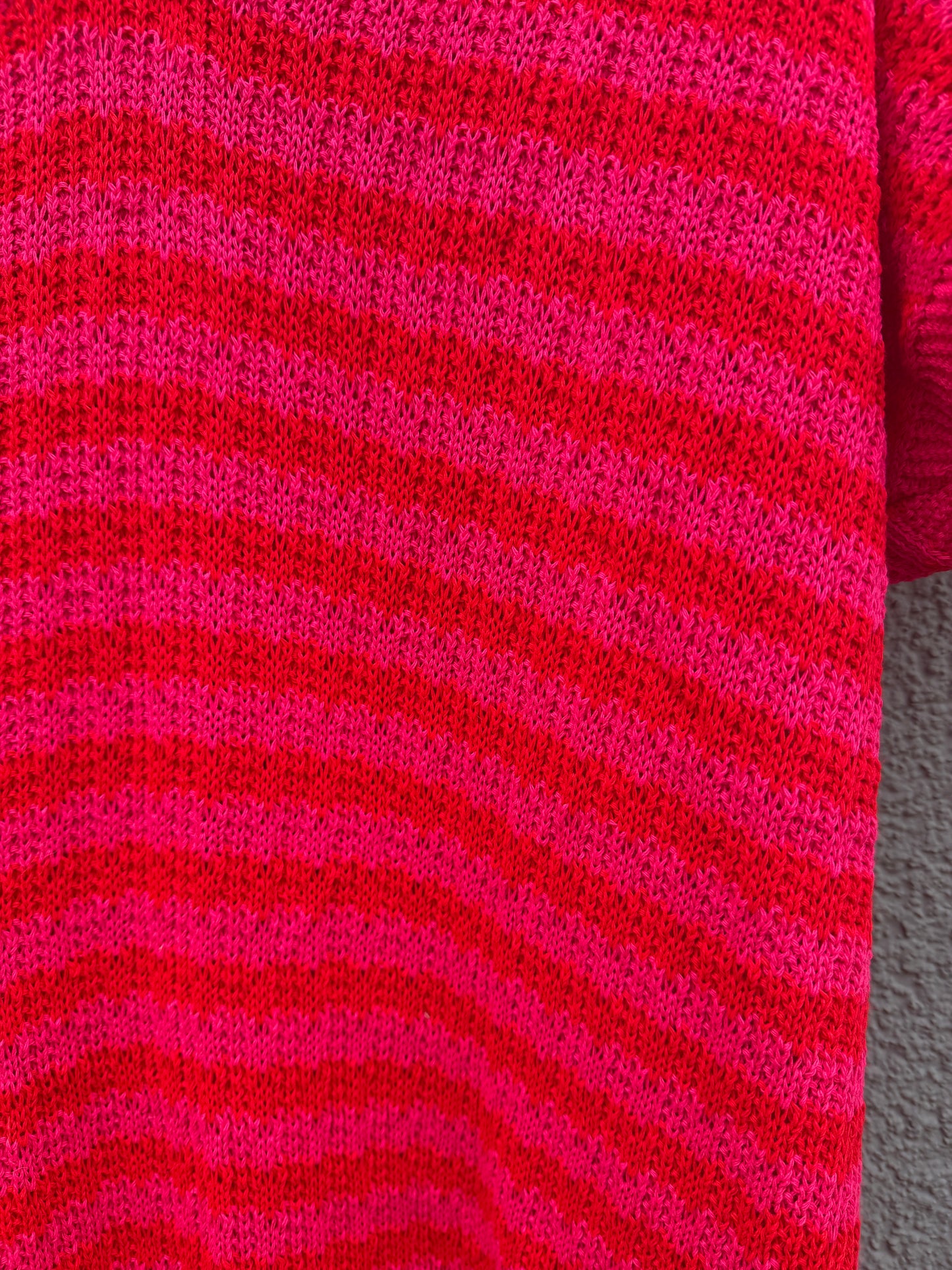 Die Nahaufnahme des Feinraummode Sommerliches Strickkleid mit Streifen pink zeigt die horizontalen rot-rosa Streifen und das strukturierte Strickmuster, das jeden leuchtenden Farbton des Garns betont.