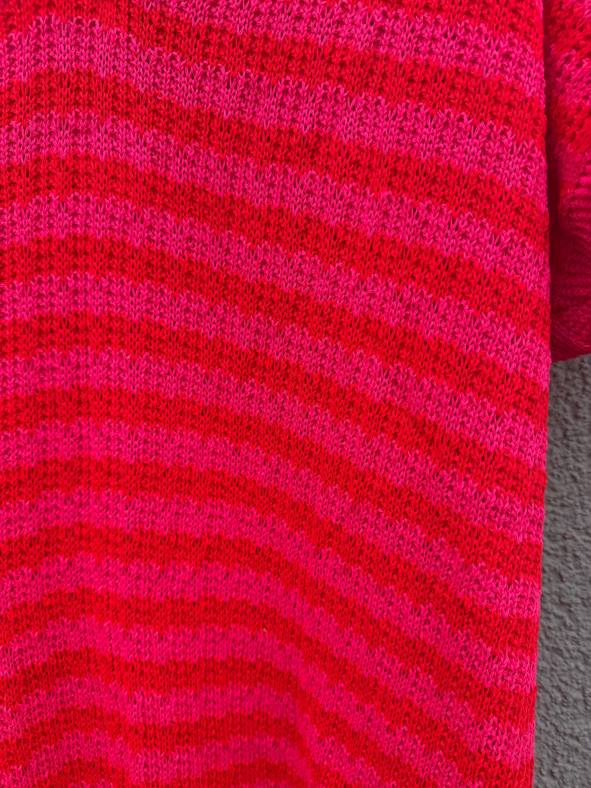 Die Nahaufnahme des Feinraummode Sommerliches Strickkleid mit Streifen pink zeigt die horizontalen rot-rosa Streifen und das strukturierte Strickmuster, das jeden leuchtenden Farbton des Garns betont.