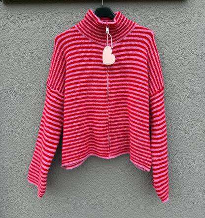 Der Gestreifter Zip Cardigan rot von Feinraummode mit pinken Streifen und hohem Kragen hängt an einem schwarzen Bügel vor einer grau strukturierten Wand.