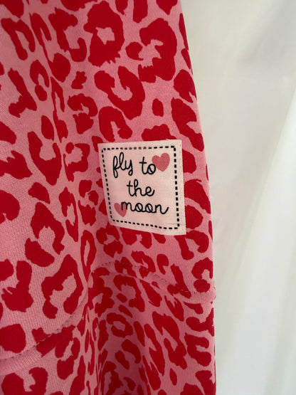 Das Oversize-Sweatshirt im Leoparden-Look - rot von Feinraummode zeigt ein rosa-rotes Leopardenmuster mit einem weißen Aufnäher mit der Aufschrift "fly to the moon" in Handschrift und einem kleinen rosa Herz in der Ecke.