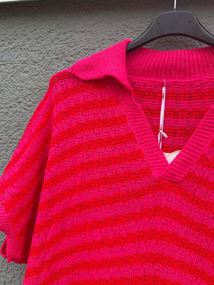 Eine Nahaufnahme des Sommerlichen Strickkleids mit Streifen pink von Feinraummode, das auf einem schwarzen Bügel vor einer grau strukturierten Wand hängt.