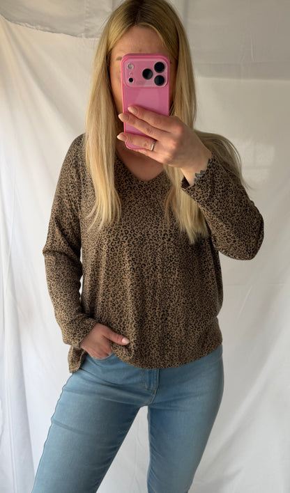 Eine Frau mit langen blonden Haaren macht ein Spiegel-Selfie in einem Feinraummode Leo Pullover Damen Animalprint - 20% Angora Wolle, gepaart mit hellblauen Jeans. Sie hält ein rosafarbenes Telefon, das ihr Gesicht teilweise verdeckt; dahinter befindet sich ein weißer Hintergrund.