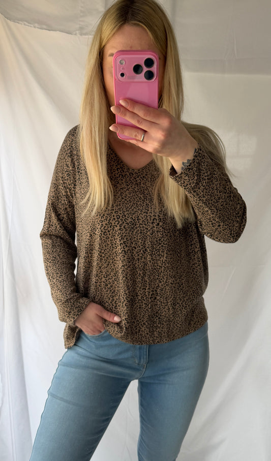 Eine Frau mit langen blonden Haaren macht ein Spiegel-Selfie in einem Feinraummode Leo Pullover Damen Animalprint - 20% Angora Wolle, gepaart mit hellblauen Jeans. Sie hält ein rosafarbenes Telefon, das ihr Gesicht teilweise verdeckt; dahinter befindet sich ein weißer Hintergrund.