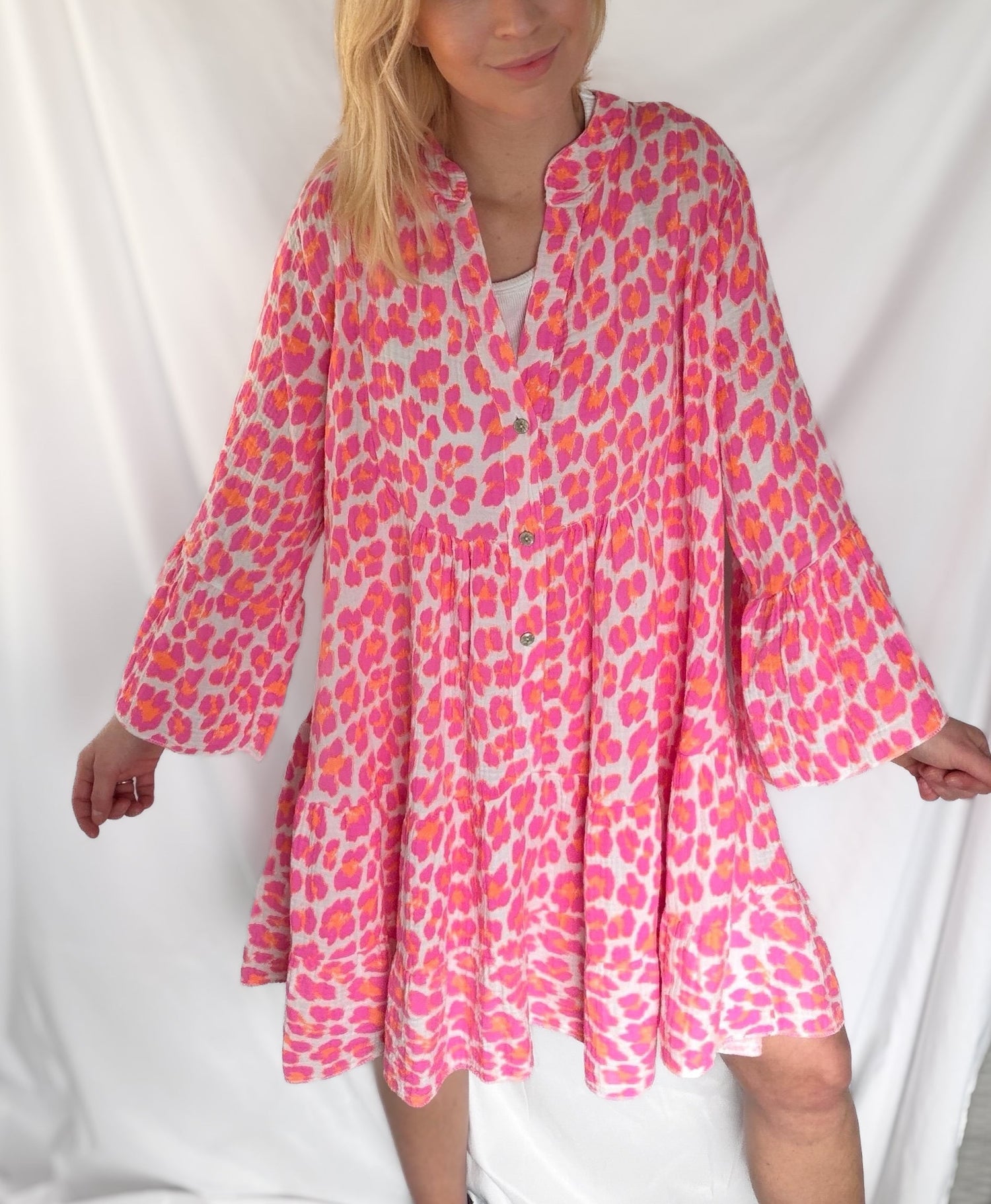 Eine Person trägt das Leo Tunika Annika von Feinraummode - ein lockeres, langärmeliges Kleid mit rosa und orangefarbenem Leo-Muster, V-Ausschnitt und einem fließenden, knielangen Rock - vor einem weißen Hintergrund.