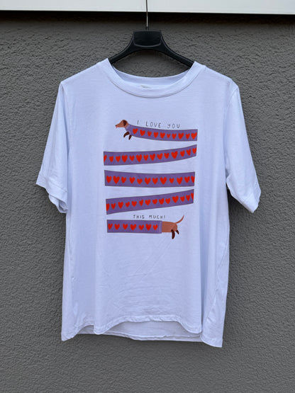 Das weiße T-Shirt mit Dackelprint & Herzen von Feinraummode zeigt einen süßen Dackel über roten Herzstreifen und dem Text "I LOVE YOU THIS MUCH!" - perfekt für Hundefans.