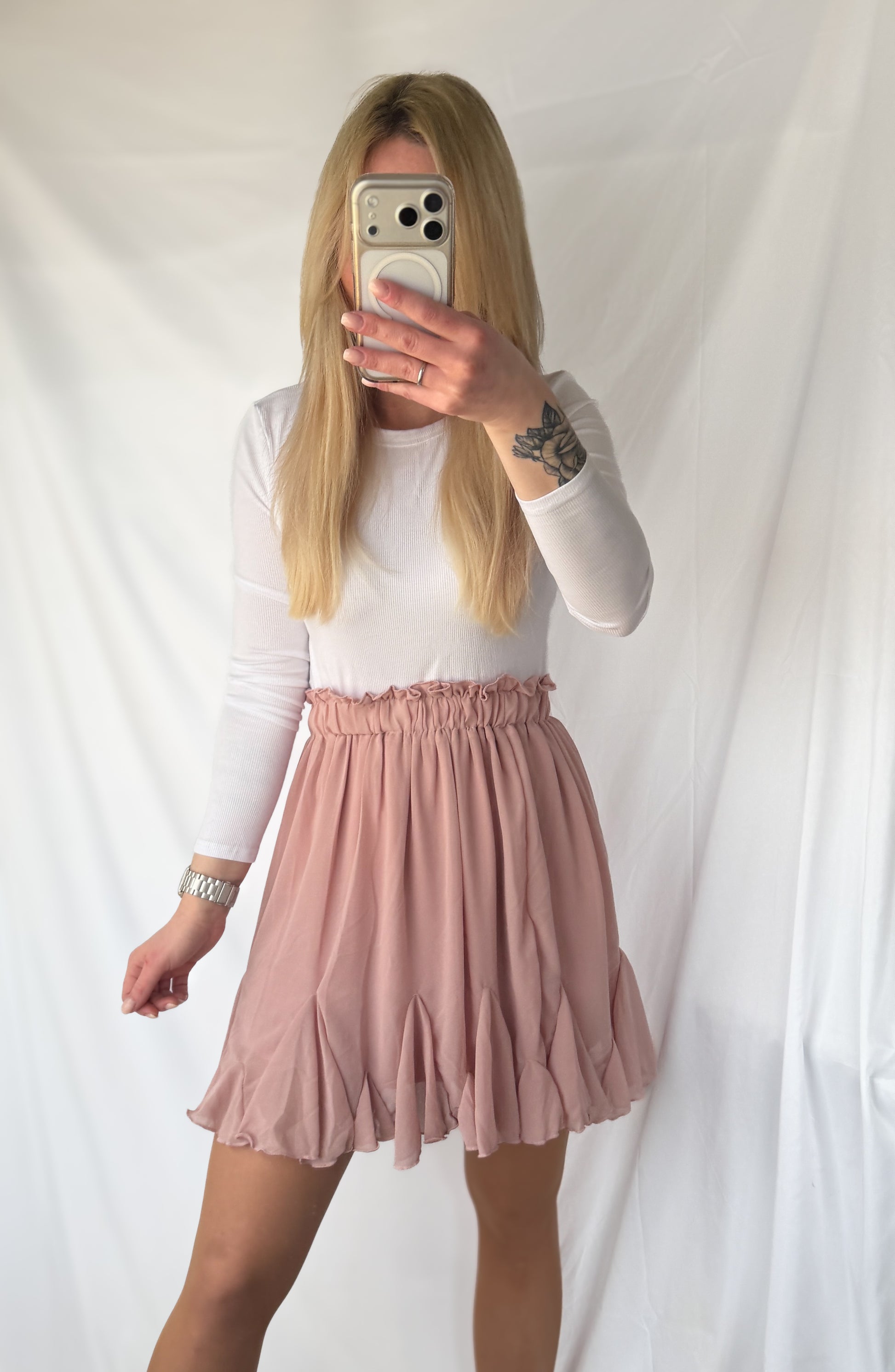 Zarter rosa Volant Rock von Feinraummode, fließender Stoff und elegante Rüschendetails, auf einem weißen Hintergrund gezeigt.