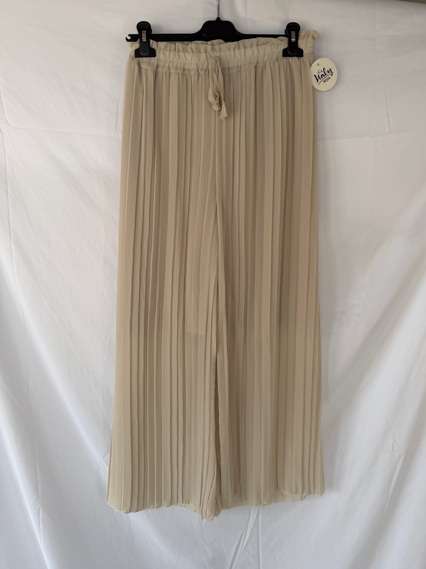 Die Plissee Hose Amanda von Feinraummode in Beige mit elastischem Taillenbund und weitem Bein hängt an einem schwarzen Bügel vor weißem Hintergrund; am Bund befindet sich ein runder, weißer Anhänger.