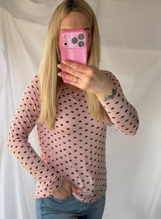 Eine Person mit langen blonden Haaren in der Feinraummode Gepunktetes Cashmere Longsleeve - Polka Dots rosa & wollweiß macht ein Spiegel-Selfie mit einem rosafarbenen Handy, ihr Gesicht teilweise verdeckt - ein schicker Moment in der zeitgenössischen Damenmode.