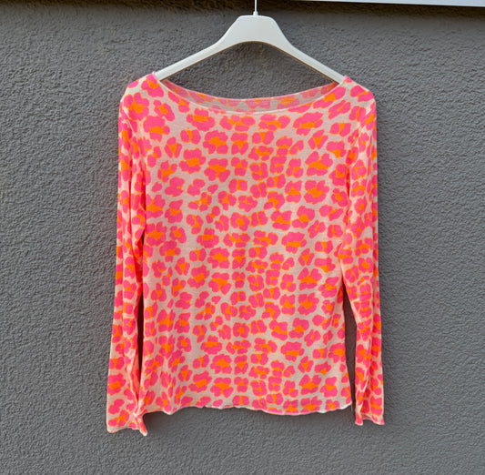 Das Feinraummode Longsleeve Leoparden Muster orange für Damen mit pink-orangem Print hängt an einem weißen Bügel vor einer grauen Wand.